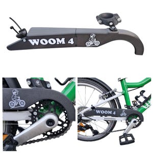 Könnte beinhalten: Schwarzer Kettenschutz mit dem Text "WOOM 4" und einer Grafik eines Kindes auf einem Fahrrad. Der Schutz soll die Kette und die Zahnräder eines Fahrrads schützen. Inklusive Montagehalterung.