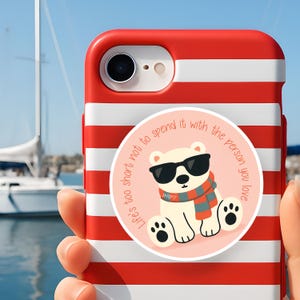 Puede incluir: Funda de teléfono a rayas rojas y blancas con una pegatina redonda que presenta un oso polar de dibujos animados con gafas de sol y una bufanda. Texto: "Life's too short not to spend it with the person you love."