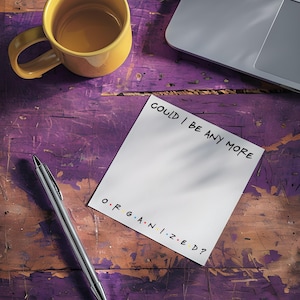 May include: A yellow mug, laptop, and pen rest on a distressed purple wooden surface. A notepad displays the text "COULD I BE ANY MORE ORGANIZED?" with the word "ORGANIZED" in colorful letters.