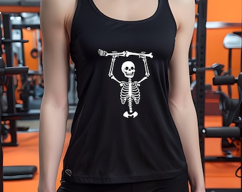 May include: Black tank top with a white skeleton graphic lifting a barbell. The athletic top has a scoop neck and is paired with black leggings. The image is taken in a gym setting with orange and black equipment.