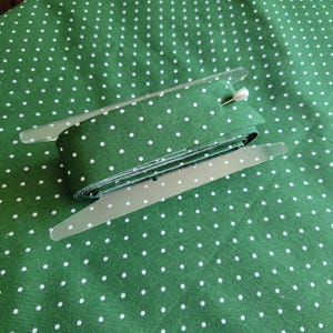 May include: A roll of green fabric with white polka dots is displayed on a clear plastic tool. The fabric is folded and ready to be used for sewing or crafting projects.