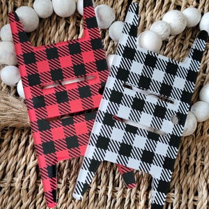 May include: Two phone grips with a buffalo plaid design. One grip is red and black, and the other is white and black.