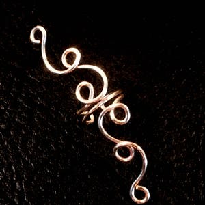 May include: A silver wire ear cuff with a spiral design. The cuff is made of thin wire that is twisted and curled into a series of loops.