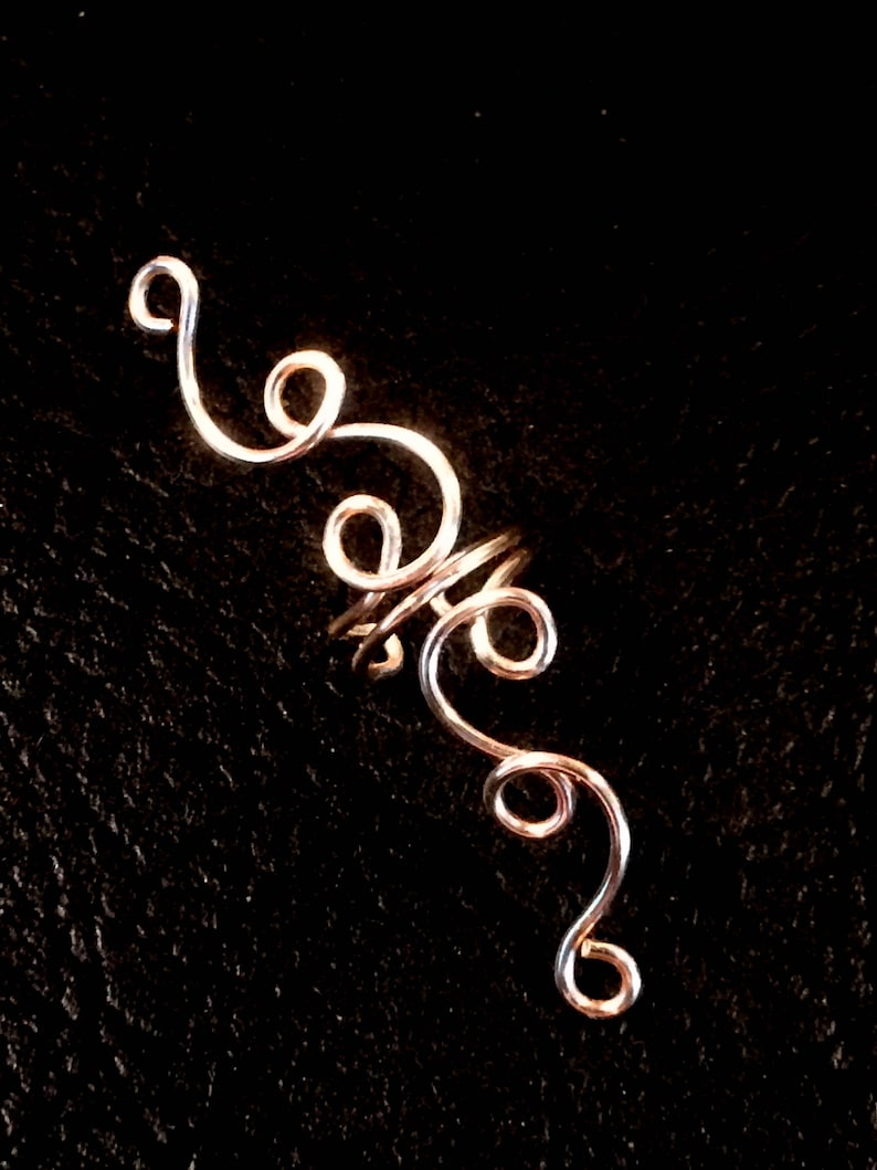 May include: A silver wire ear cuff with a spiral design. The cuff is made of thin wire that is twisted and curled into a series of loops.