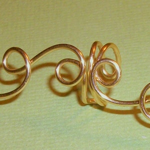 May include: Gold wire ear cuff with a swirling design. The cuff is made of a single piece of wire that is twisted and shaped into a decorative pattern.