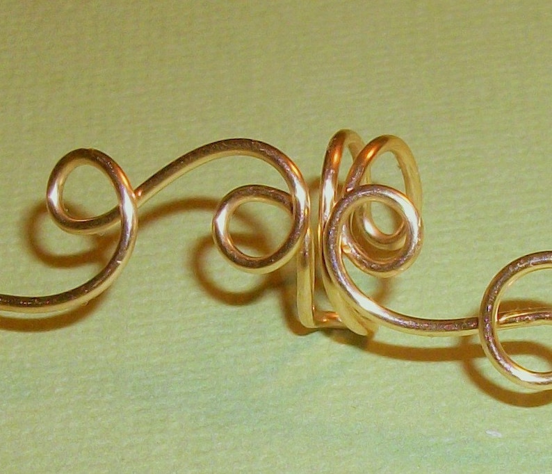 May include: Gold wire ear cuff with a swirling design. The cuff is made of a single piece of wire that is twisted and shaped into a decorative pattern.