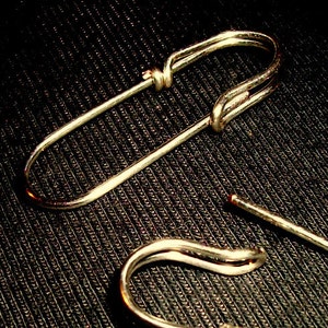 May include: Two silver safety pins, one open and one closed, on a black textured background.