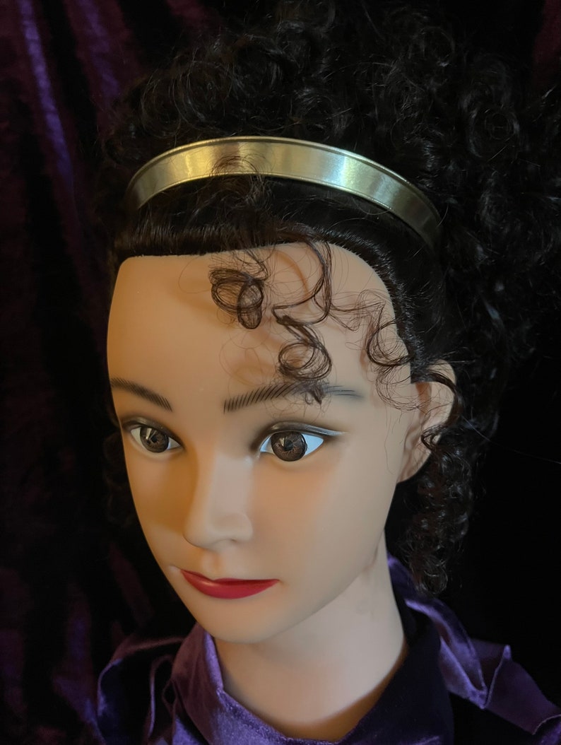 May include: A silver headband with a smooth, shiny finish. The headband is worn on a mannequin with curly brown hair.