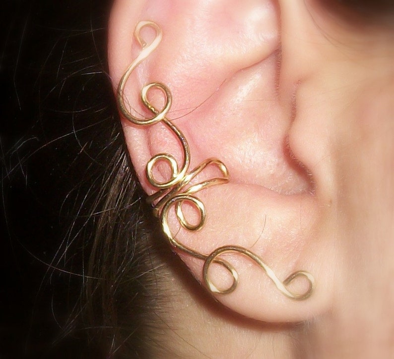 May include: A gold ear cuff with a delicate, intricate design. The cuff is made of thin wire that is twisted and curled into a floral pattern. It is a beautiful and unique piece of jewelry that would add a touch of elegance to any outfit.