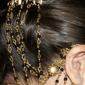 May include: A gold hair comb with black beads and a white pearl-like accent. The comb is worn in a woman's hair, with the beads cascading down the side of her head.