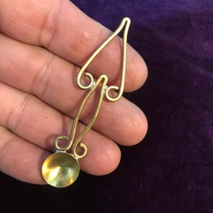 Puede incluir: Una cuchara de metal de color dorado con un cuenco redondeado y un mango decorativo. El mango tiene forma de árbol estilizado con dos ramas.