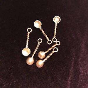 May include: Six small, silver-coloured spoons with twisted handles. The spoons are arranged in a cluster on a dark purple surface.