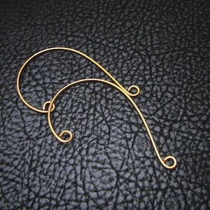May include: A pair of gold wire earrings with a curved shape and a small loop at the end of each wire.