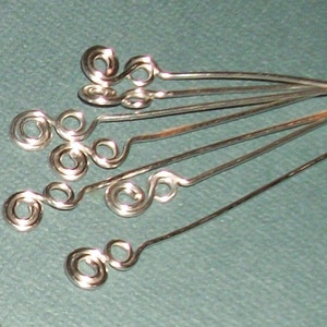 Puede incluir: Primer plano de hallazgos de joyer&iacute;a de alambre plateado con m&uacute;ltiples bucles y remolinos. Los hallazgos est&aacute;n dispuestos en forma de abanico.