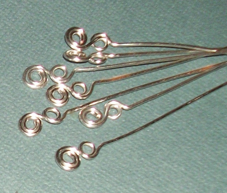 Puede incluir: Primer plano de hallazgos de joyer&iacute;a de alambre plateado con m&uacute;ltiples bucles y remolinos. Los hallazgos est&aacute;n dispuestos en forma de abanico.