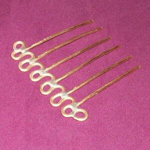 May include: A gold hair comb with seven teeth, each ending in a double loop. The comb is made of a textured metal.