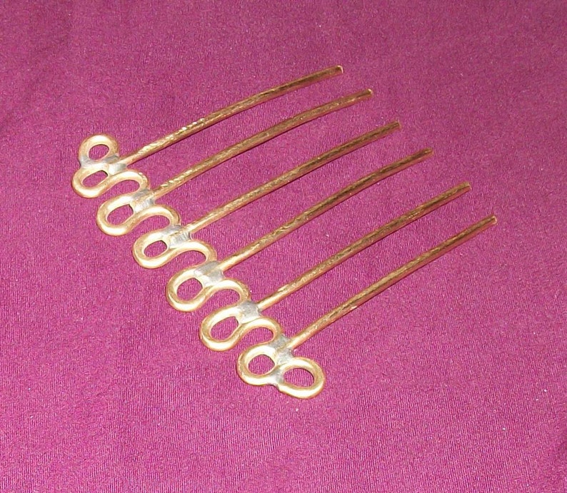 May include: A gold hair comb with seven teeth, each ending in a double loop. The comb is made of a textured metal.