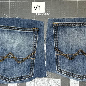 Könnte beinhalten: Zwei Jeans-Hosentaschen mit Used-Look. Jede Tasche hat eine dekorative Zickzacknaht in einer kontrastierenden Goldfarbe. Die Taschen sind aus einem größeren Stück Jeansstoff geschnitten. Der Text "V1" und "FISKARS" ist sichtbar.