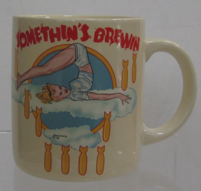 Pode incluir: Caneca de cer&acirc;mica creme com uma al&ccedil;a. A caneca apresenta uma ilustra&ccedil;&atilde;o retr&ocirc; de uma mulher em pose de ioga em uma nuvem, cercada por bombas de desenho animado. O texto "SOMETHIN'S BREWIN" &eacute; impresso em vermelho.