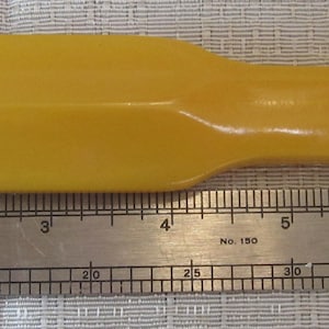 Può includere: Oggetto rettangolare giallo con manico, possibilmente un utensile o parte di esso. Un righello di metallo con segni in centimetri è posto accanto all'oggetto. L'oggetto misura circa 20 cm di lunghezza.