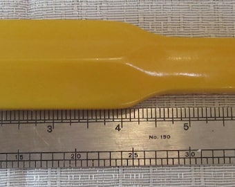 May include: A solid yellow, rectangular object with a handle, possibly a tool or part of a tool. A metal ruler with inch markings is placed next to the object. The object appears to be approximately 8 inches long.