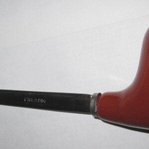 May include: A letter opener featuring a smooth, glossy, dark reddish-brown handle shaped like a tobacco pipe. The blade is made of polished silver-toned metal and is engraved with the text "LUMINA" near the handle connection point.