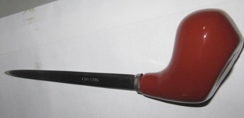 May include: A letter opener featuring a smooth, glossy, dark reddish-brown handle shaped like a tobacco pipe. The blade is made of polished silver-toned metal and is engraved with the text "LUMINA" near the handle connection point.