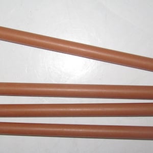Può includere: Quattro tasselli cilindrici marroni di diverse lunghezze sono disposti su una superficie bianca. I tasselli sono di un colore solido e uniforme e sembrano essere fatti di legno o materiale simile. I tasselli sono dritti e hanno estremità arrotondate.