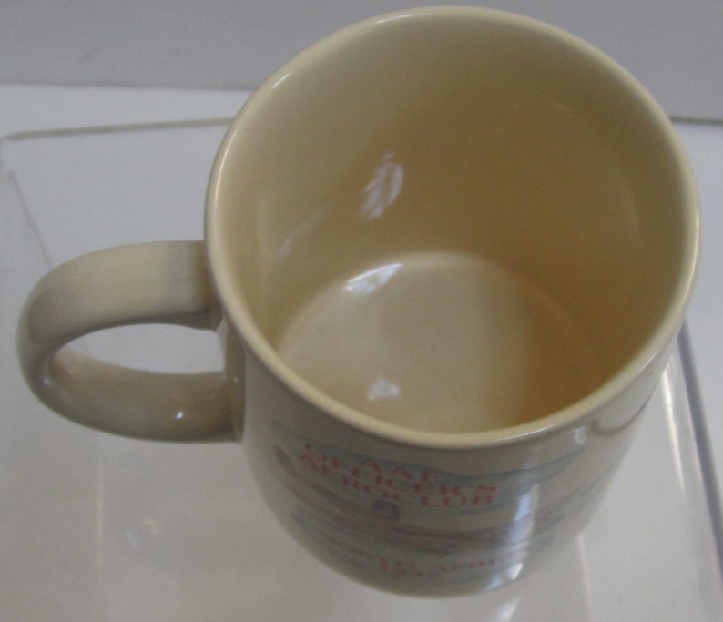 Pode incluir: Caneca de cer&acirc;mica creme com uma al&ccedil;a curva. O interior &eacute; um tom de creme mais claro. A caneca tem texto e um gr&aacute;fico na lateral. A caneca foi projetada para bebidas quentes.