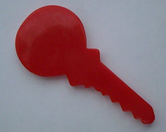 May include: A bright red, flat, key-shaped object with a smooth, rounded head and a jagged, serrated blade edge. The item features a solid, uniform color throughout its entire surface, presenting a simple, stylized silhouette of a standard key.