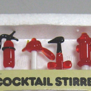 May include: A set of four glass cocktail stirrers in a white foam tray, featuring miniature red and black fire-themed shapes including a fire extinguisher, a fire helmet, an axe, and a fire hydrant. The box is labelled 4 COCKTAIL STIRRERS.