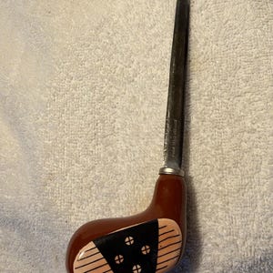 May include: A letter opener featuring a metal blade attached to a handle shaped like a brown golf club head. The handle has a black center panel with four circular accents and thin horizontal lines on the light tan sides. The blade is marked Stainless Steel Korea.