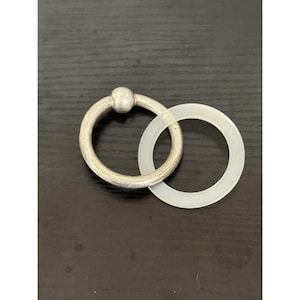 May include: A silver-toned metal ring featuring a small spherical accent at the top, interlocked with a secondary, thinner, translucent white circular ring. The metal ring has a matte, textured finish, while the white ring appears smooth and semi-clear.