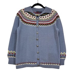 Könnte beinhalten: Hellblauer Cardigan mit Kragen und Knopfleiste. Der Pullover hat ein detailliertes geometrisches Muster in Rot, Gelb, Weiß und Schwarz auf Brust und Ärmeln. Die Manschetten und der Saum haben ebenfalls ein Muster.