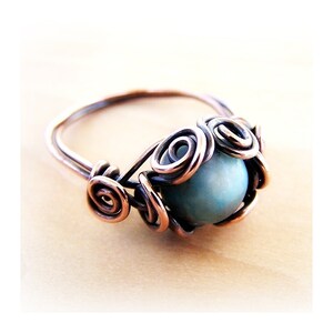 May include: A copper wire ring with a blue and white stone set in the center. The stone is surrounded by copper wire swirls.