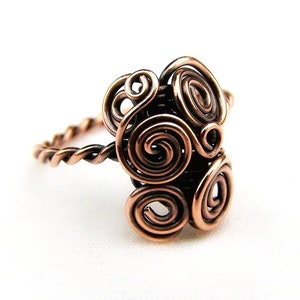 May include: A copper wire ring with a swirling, abstract design. The ring is made of twisted wire and has a unique, handmade look.