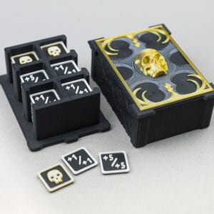 Può includere: Accessori per giochi da tavolo neri e dorati. Include una scatola con un teschio sopra, un porta carte con gettoni a teschio e diversi piccoli gettoni quadrati con grafiche di teschi e numeri. Gli articoli sono in plastica.