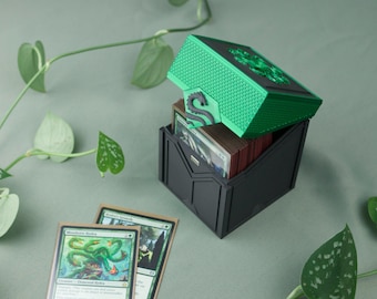 May include: A black and green card storage box with a dragon design on the lid. The box is open, revealing a stack of cards. Two cards are in front of the box, with green and blue illustrations.