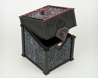 May include: A black box with a hinged lid, featuring a gray brick-patterned base and a top panel decorated with a red skull relief. The lid has a smaller red skull emblem on the front edge, and the sides are adorned with intricate black scrollwork.