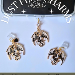 May include: Three gold-toned metal dragon charms with black and white enamel detailing. Each charm features a dragon with spread wings and intricate patterns. One charm includes a small clear crystal accent, and another has a black heart charm.