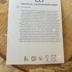 Op de afbeelding: Een witte kaart met zwarte tekst, getiteld "Gebrauchs- und Sicherheitshinweise" (Gebruiks- en veiligheidsinstructies). De kaart bevat veiligheidswaarschuwingen en instructies voor 3D-geprinte producten, met pictogrammen en een waarschuwingssymbool.