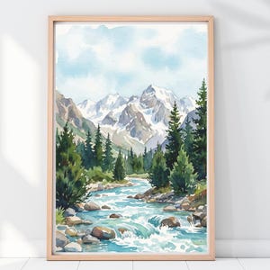 May include: Watercolor painting of a mountain landscape with a river flowing through a forest. The artwork features snow-capped mountains, evergreen trees, and a light blue sky. The painting is framed in a light brown wooden frame.