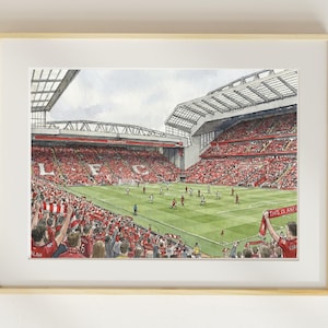 May include: Watercolor print of a soccer stadium filled with fans in red. The field is green, and the sky is overcast. The letters "LFC" are visible. The artwork is framed in a light wood frame.