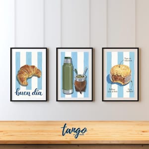 Puede incluir: Tres impresiones enmarcadas con un fondo a rayas azul claro y blanco. La impresión de la izquierda muestra un cruasán con el texto "buen dia". La impresión del medio representa un termo verde y una calabaza marrón con una pajita de metal. La impresión de la derecha muestra un alfajor.