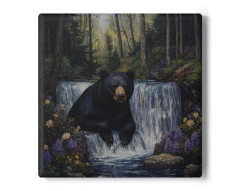 Puede incluir: Impresión en lienzo cuadrada que muestra un oso negro descansando cerca de una cascada. El oso tiene un hocico marrón y está rodeado de exuberante vegetación, incluyendo flores moradas y amarillas. El fondo muestra un bosque.