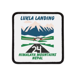 May include: A white patch with black stitching featuring a colourful illustration of a plane landing on a runway with the text "LUKLA LANDING" and "HIMALAYA MOUNTAINS NEPAL" and the number "24" on the runway.