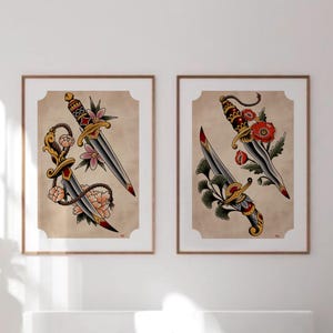 May include: Two framed art prints featuring traditional tattoo-style illustrations of daggers. Each dagger has a silver blade, ornate gold handle, and is adorned with colorful flowers and leaves. The background is a tan color.