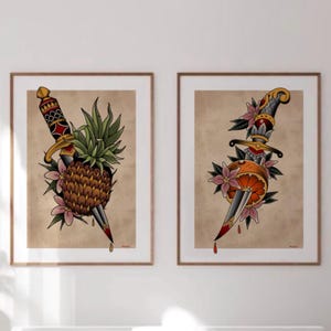 May include: Two framed art prints featuring traditional tattoo-style illustrations. One shows a dagger piercing a pineapple, the other a dagger through an orange. Both are surrounded by flowers and leaves, with a vintage paper background.