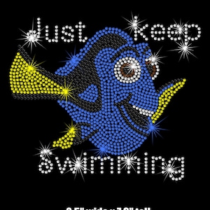 May include: A blue and black cartoon fish with a yellow fin, surrounded by sparkling rhinestones, with the text "Just Keep Swimming" in white rhinestones. The image is 8.5 inches wide and 7.3 inches tall.