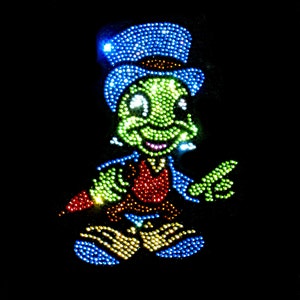 May include: A green and blue cartoon character with a top hat, wearing a red vest and blue pants. The character is made of rhinestones and is smiling.
